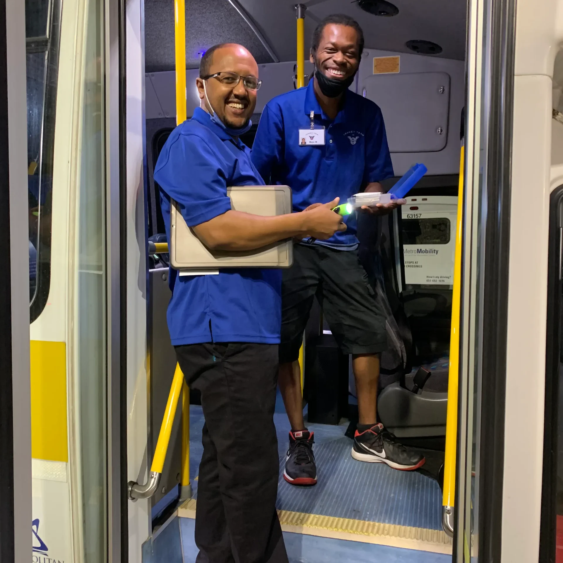 two employees in blue shirts standing in the entrance of a bus