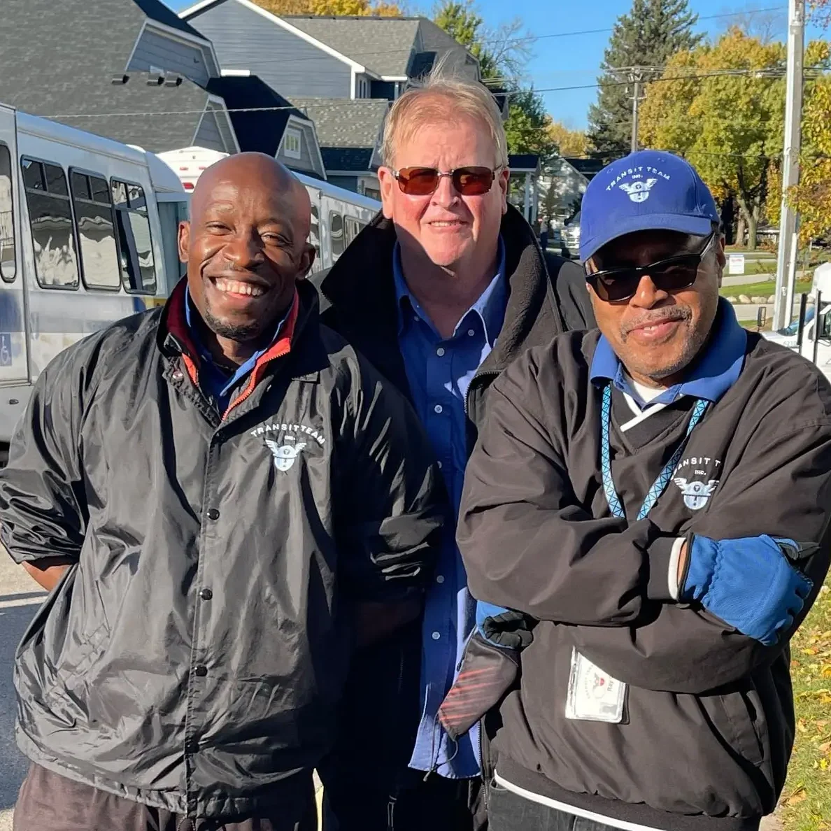 three men outside smiling with busses in the background